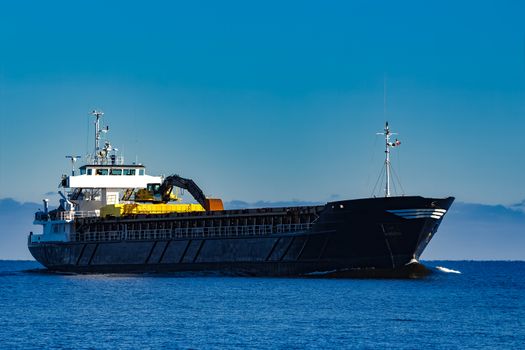 Black cargo ship with long reach excavator moving by baltic sea