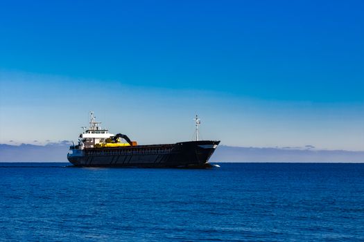 Black cargo ship with long reach excavator moving by baltic sea