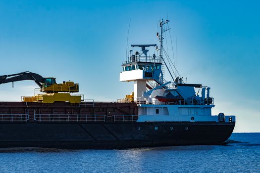 Black cargo ship with long reach excavator moving by Baltic sea