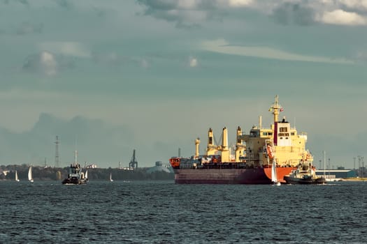 Red cargo ship and the tug ship towing it to the port