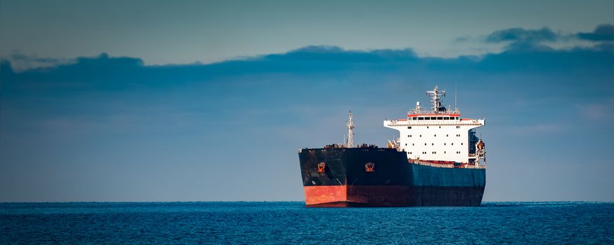 Black cargo ship moving in still Baltic sea water. Riga, Europe