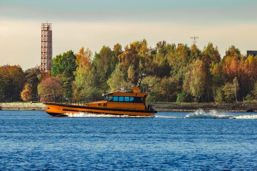 Orange pilot ship sailing past the autumn trees in Europe