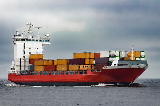 Red cargo container ship sailing from Baltic sea in cloudy day