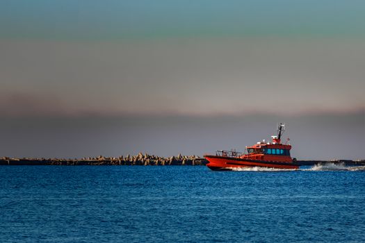 Red pilot ship moving past the breakwater dam in Riga, Europe