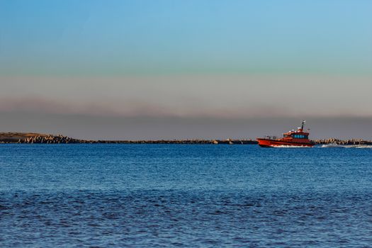 Red pilot ship moving past the breakwater dam in Riga, Europe