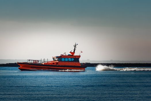 Red pilot ship moving at speed past the breakwater dam