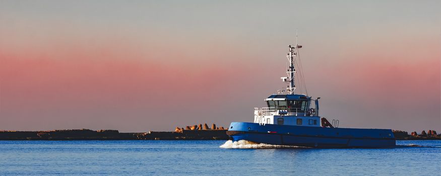 Blue small tug ship sailing past the breakwater dam in morning