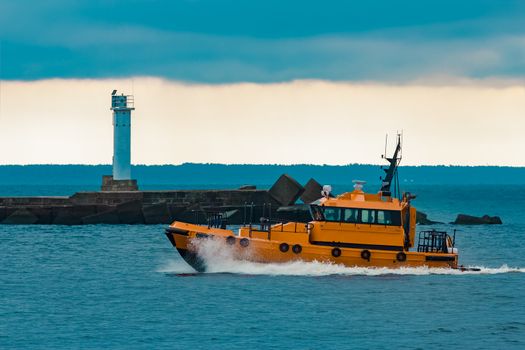 Orange pilot ship moving at speed past the lighthouse in Riga