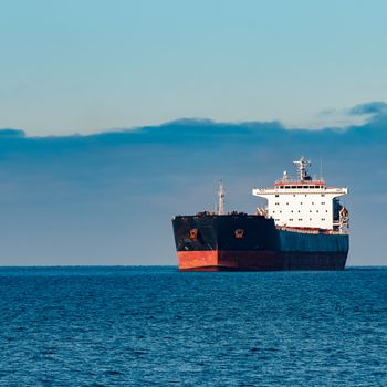 Black cargo ship moving in still Baltic sea water. Riga, Europe