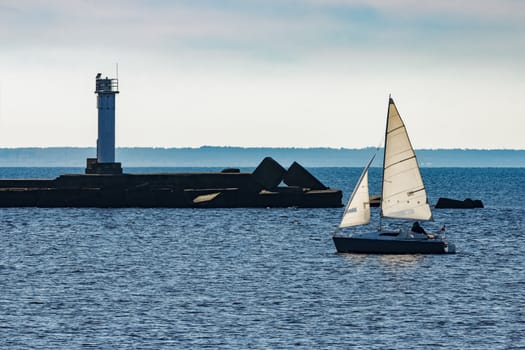 Small sailboat traveling past the lighthouse in sunny day