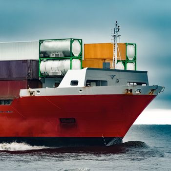 Red cargo container ship's bow in cloudy day