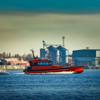 Red pilot ship moving past the factory in Latvia