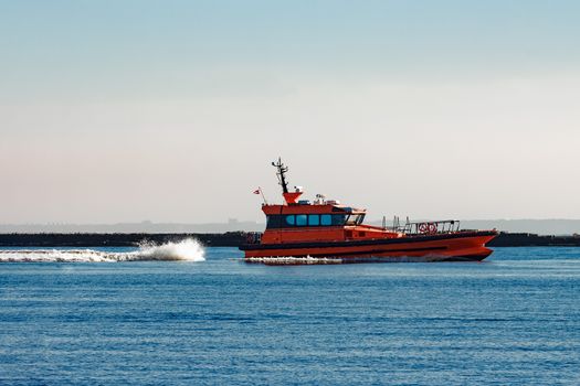 Red pilot ship moving at speed past the breakwater dam
