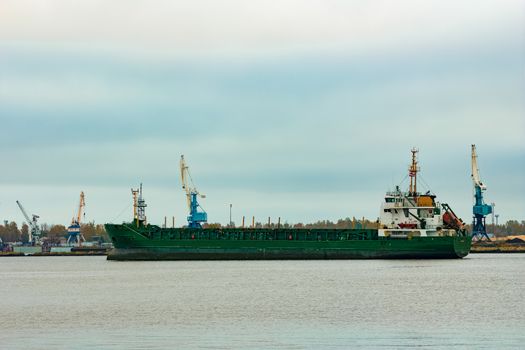 Green cargo ship moving to the port in cloudy day