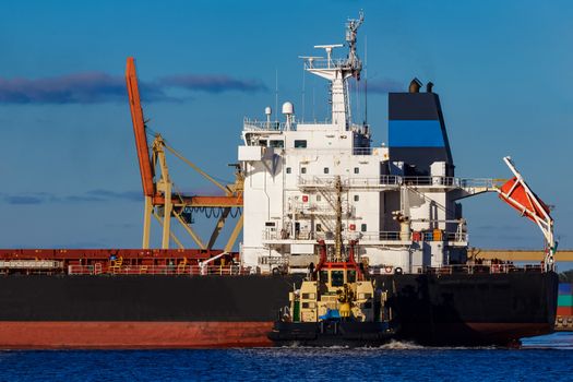 Black cargo ship mooring at the port with tug ship support