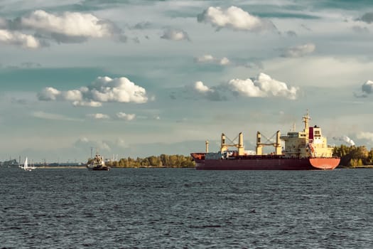 Red cargo ship and the tug ship guide it to the port