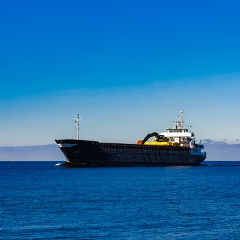 Black cargo ship with long reach excavator moving by baltic sea