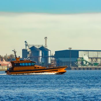 Orange pilot ship sailing past the factory in Latvia