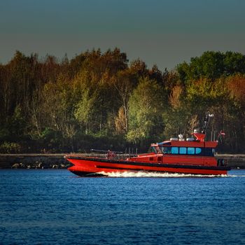 Red pilot ship moving past the autumn trees in Europe