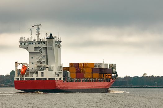 Red cargo container ship entering the port of Riga in cloudy day