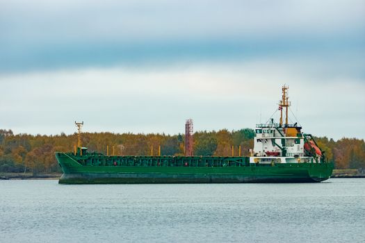 Green cargo ship moving to the port in cloudy day