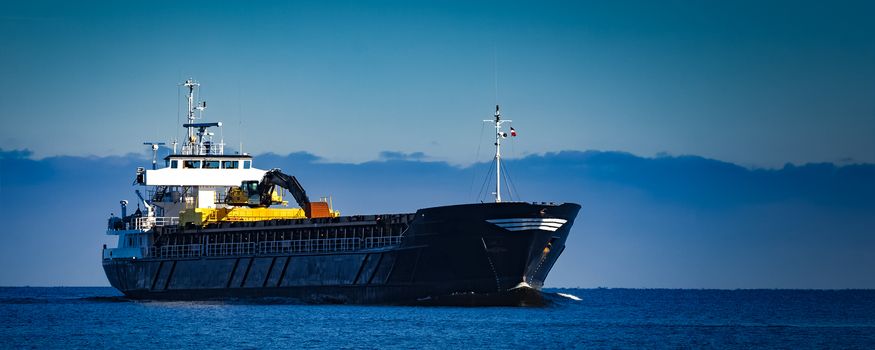 Black cargo ship with long reach excavator moving by baltic sea