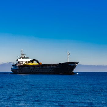 Black cargo ship with long reach excavator moving by baltic sea