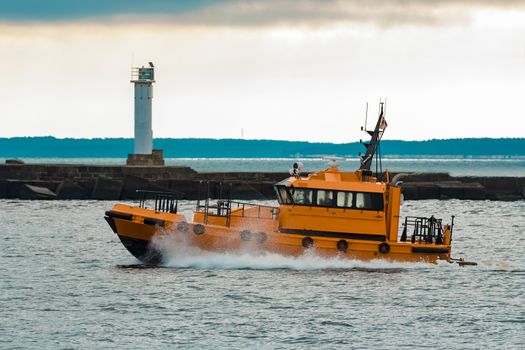 Orange pilot ship moving at speed past the lighthouse in Riga