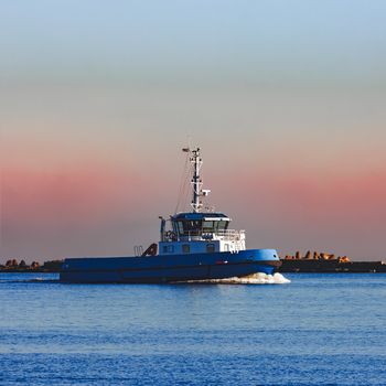 Blue small tug ship sailing past the breakwater dam in morning