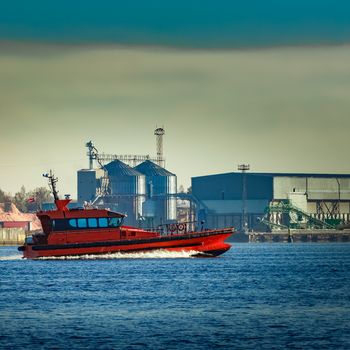 Red pilot ship moving past the factory in Latvia