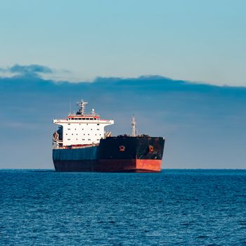 Black cargo ship moving in still Baltic sea water. Riga, Europe