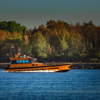 Orange pilot ship sailing past the autumn trees in Europe