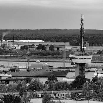 Military ship sailing past the cargo port in Latvia. Monochrome