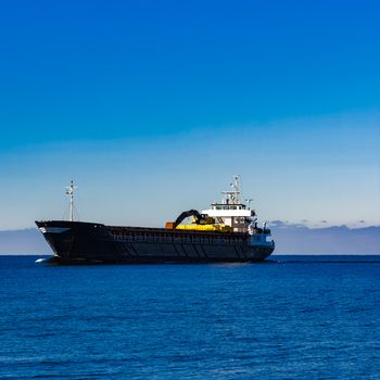 Black cargo ship with long reach excavator moving by baltic sea