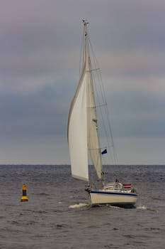 White sailboat traveling in Baltic sea in cloudy day