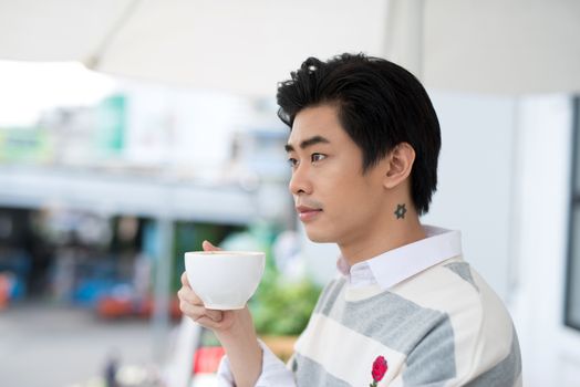 Handsome young man drinking coffee looking out at the view from his home office 