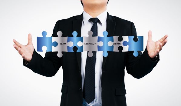 Business man showing  jigsaw puzzle  with team strategy vision wording. concept for business isolated on white background