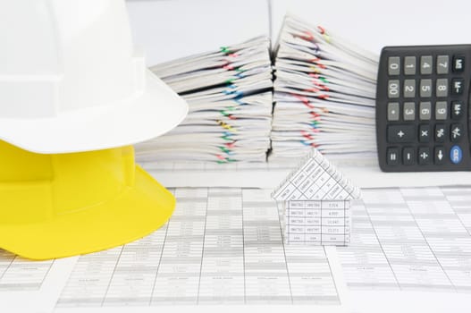 House and white on yellow engineer hat on finance account have blur pile overload document of report and receipt with colorful paperclip with calculator place vertical as background.