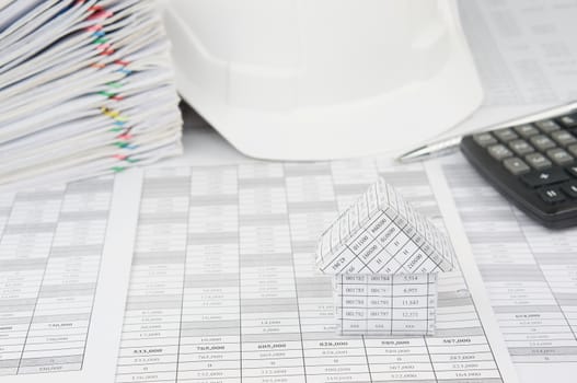 House on finance account have blur white engineer hat and pile overload document of report and receipt with colorful paperclip with calculator and pen as background.