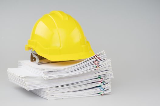 Pile overload document of report and receipt with colorful paperclip have yellow engineer hat on top with white background.