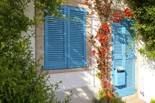 Typical Mediterranean house with white walls and blue fixtures. Boungaville flowers frame the windows.