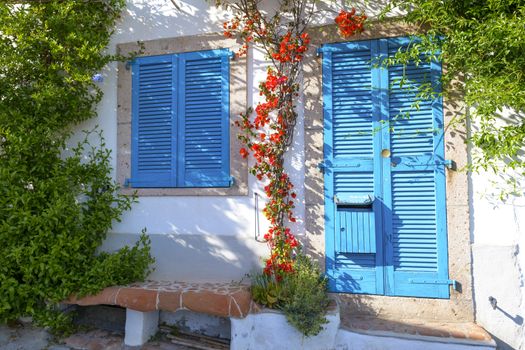Typical Mediterranean house with white walls and blue fixtures. Boungaville flowers frame the windows.