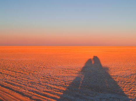 Shimmering horizon and long shadows as sun sets across Makgadikgadi Pans National Park, scenic large flat area of salt pan desert of Botswana