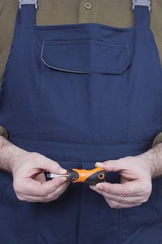 Screwdriver in the hands of a mechanic dressed in overalls