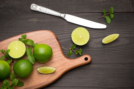 Fresh limes on cutting board on wooden table. Top view, background.