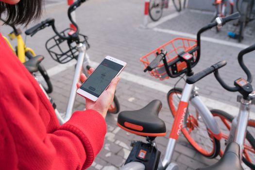 A young woman  is looking at smart phone to find her bicycle