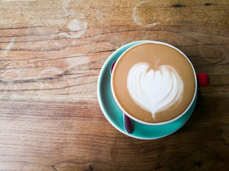 A red cup of coffee with heart pattern on wooden background