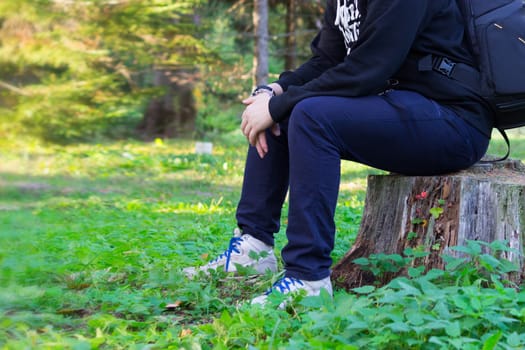Young man with backpack sitting on stump in the forest