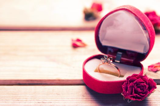 Golden engagement ring in a heart shaped box and roses