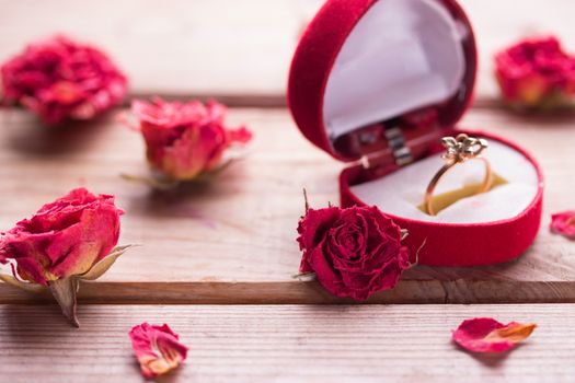 Golden engagement ring in a heart shaped box and roses